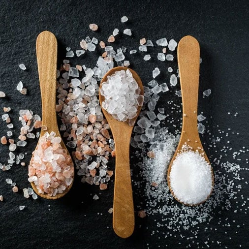 Wooden spoon with different size salts scooped into them.